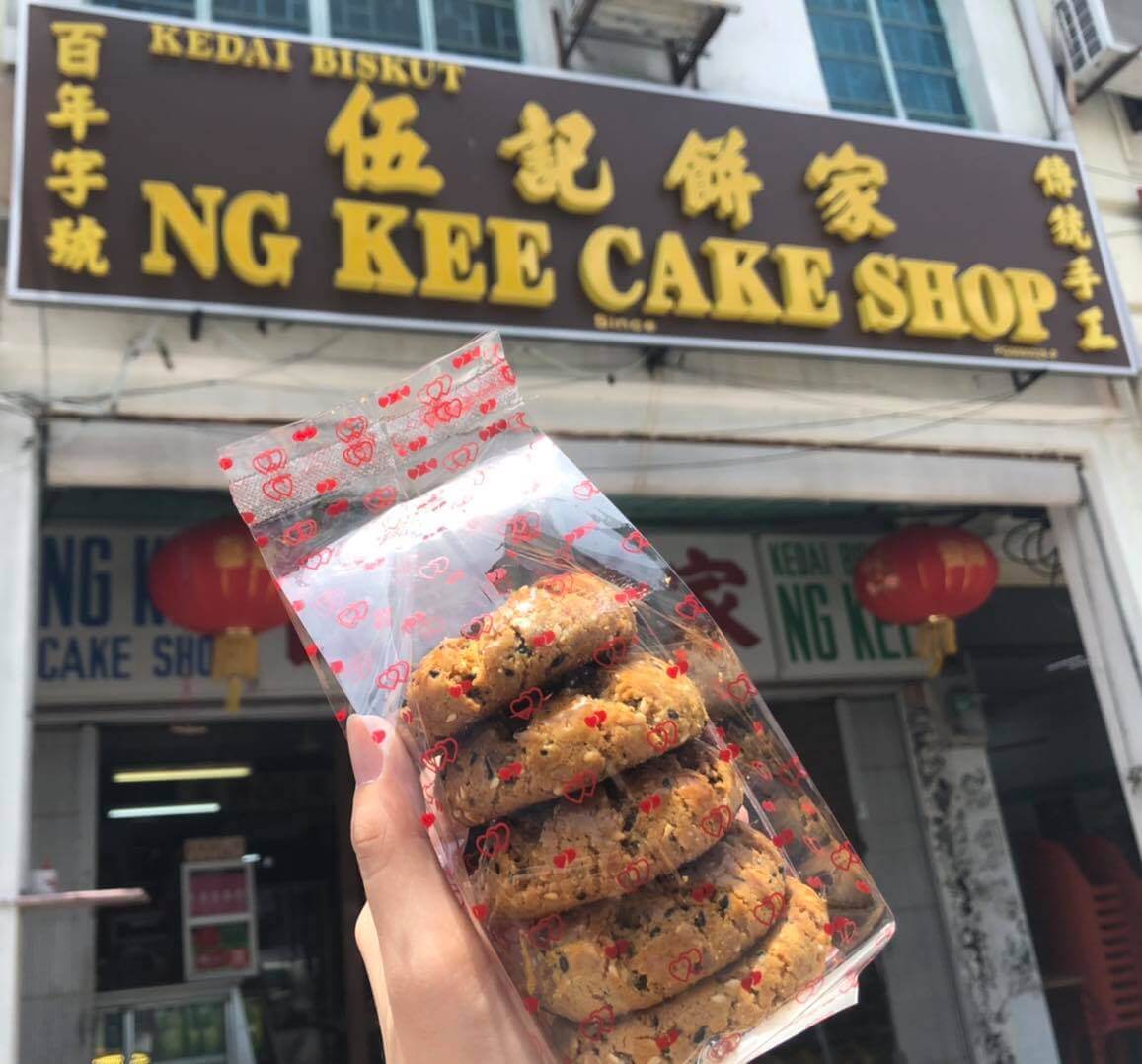 a hand holding traditional chinese biscuit in front of the biscuit shop