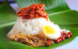 white rice with anchovies, fried peanuts, hard boiled egg and curry served on a banana leaf