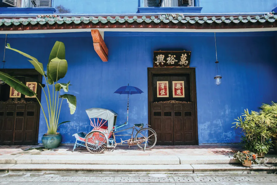 trishaw in front of a building with indigo colours walls and traditional wooden door with Chinese wordings
