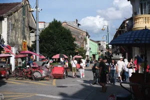 people walking along a street with old shophouses and trishaws