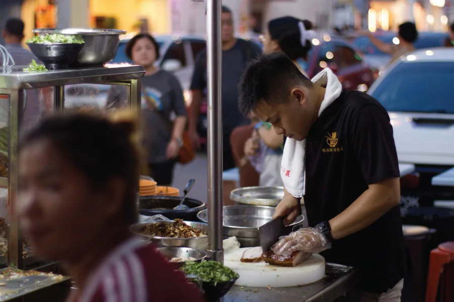 a man cutting a cooked food at a stall by the street