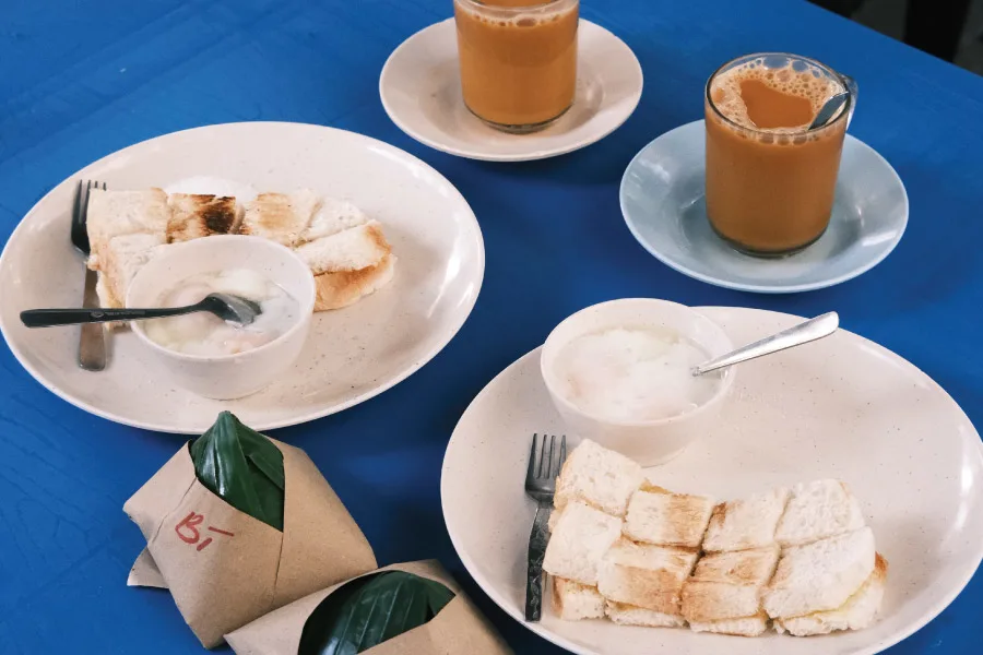 roti bakar, packs of Nasi lemak and teh Tarik served on a table