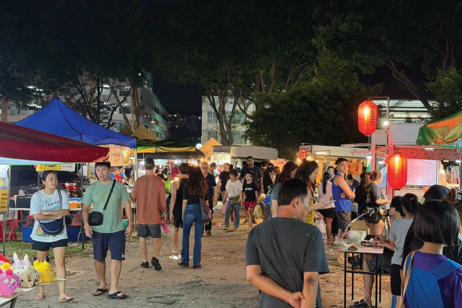 crowd walking around makeshift stalls on a field at night