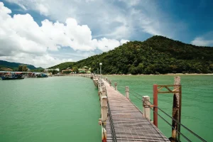 a wooden dock over the sea with a hill at the background